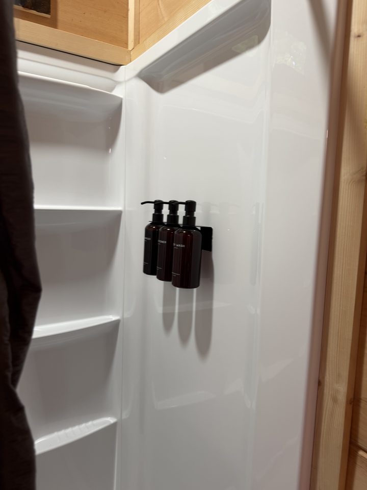 Three refillable amber pump bottles of shampoo, conditioner and body wash in a black bracket inside the shower