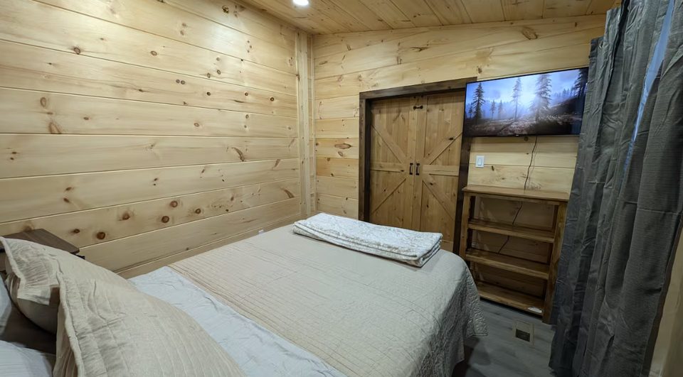 Queen bedroom with pine walls, wall-mounted television and a sliding barn door