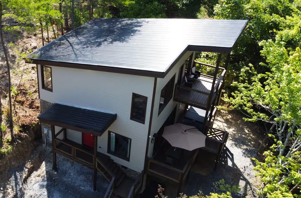 The chalet seen from above, standing-seam roof and deck surrounded by woodland