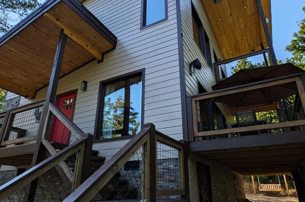 Modern chalet with angular rooflines, red front door and stacked timber decks, set among trees