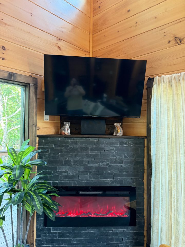 Stone fireplace with a linear flame and a television above, tall window alongside