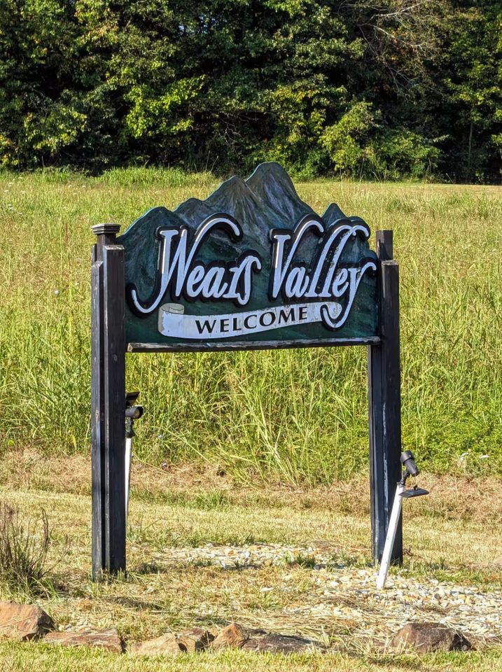 Carved roadside sign reading Wears Valley Welcome in a grassy verge